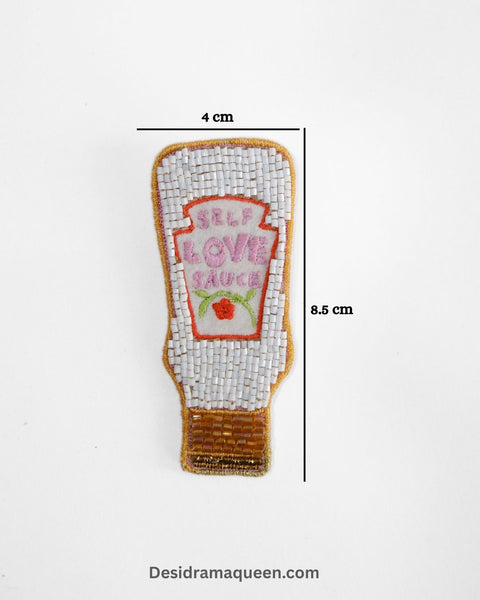 White and red embroidered brooch shaped like a sauce bottle