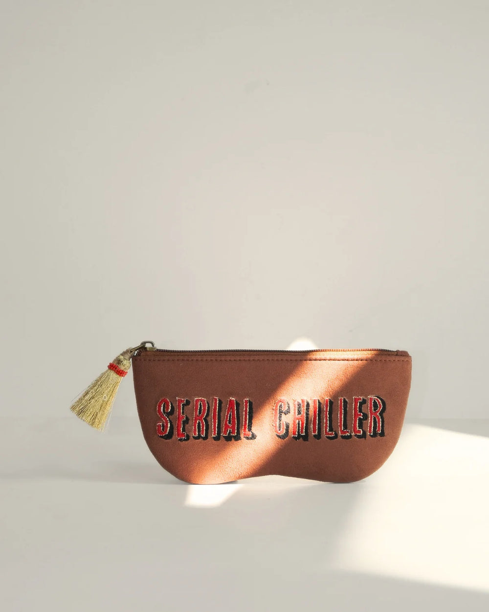 Brown pouch with 'Serial Chiller' text and tassel on a light gray background