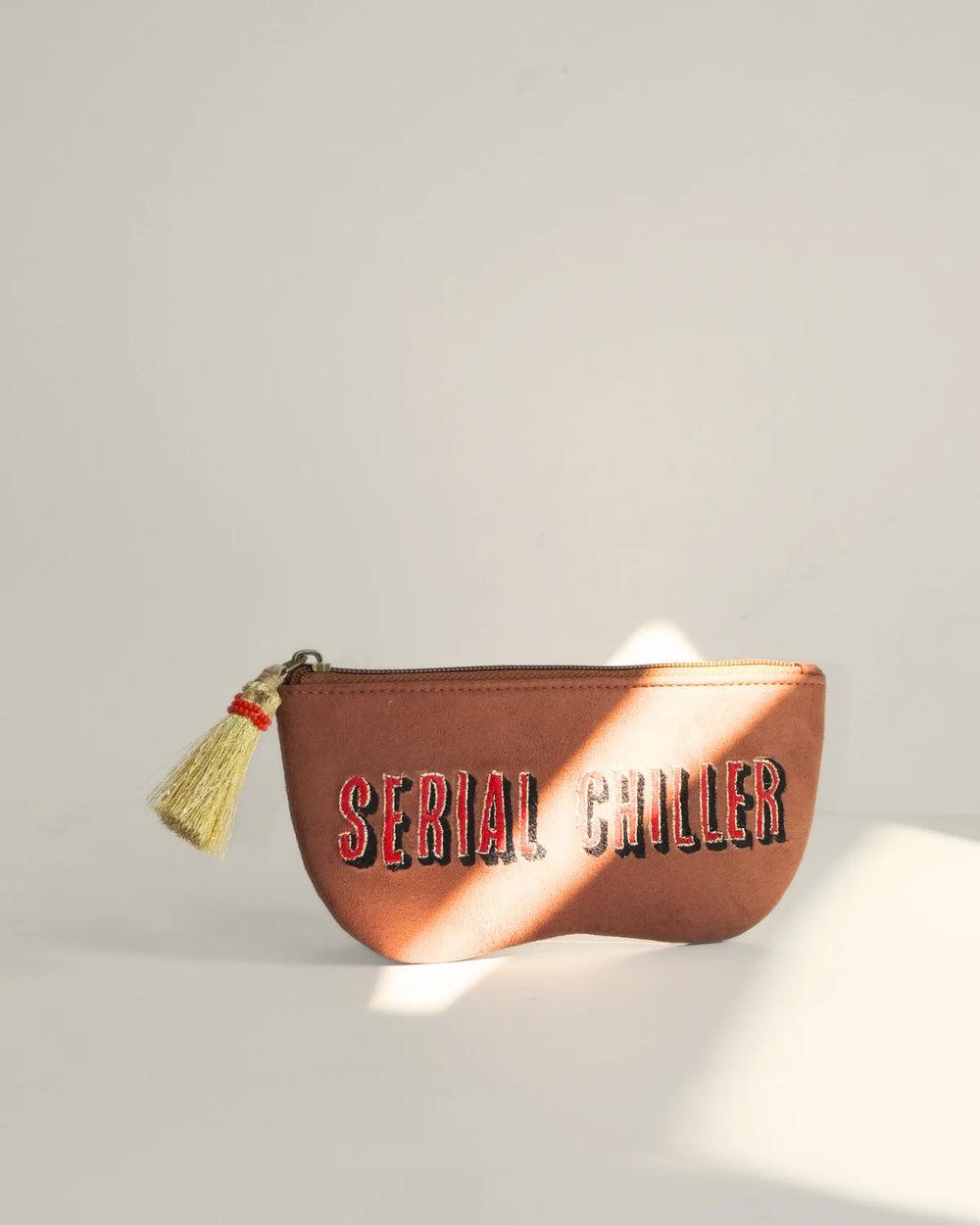 Brown pouch with 'Serial Chiller' text and tassel on a light gray background