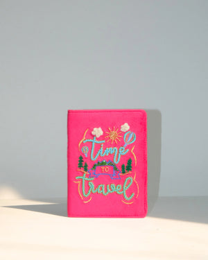 Pink passport holder with 'Time to Travel' embroidery on a gray background