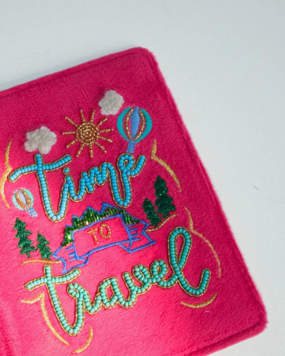 Pink passport holder with 'Time to Travel' embroidery on a gray background