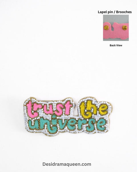 Handmade embroidered brooch with the motivational text ‘Trust the Universe’ in pink, yellow, teal, and white beads