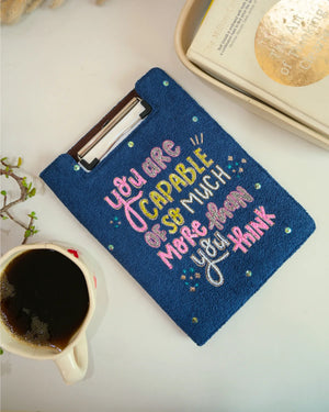Blue pouch with motivational quote next to a cup of coffee on a light surface