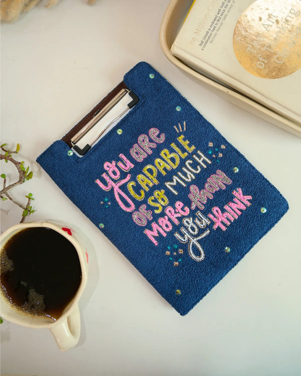 Blue pouch with motivational quote next to a cup of coffee on a light surface