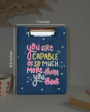 Blue clipboard with motivational quote, dimensions indicated, on a neutral background