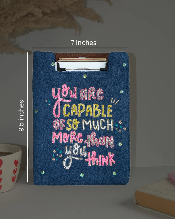 Blue clipboard with motivational quote, dimensions indicated, on a neutral background