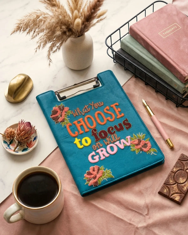 Blue clipboard with motivational quote, coffee cup, and decorative items on a table.