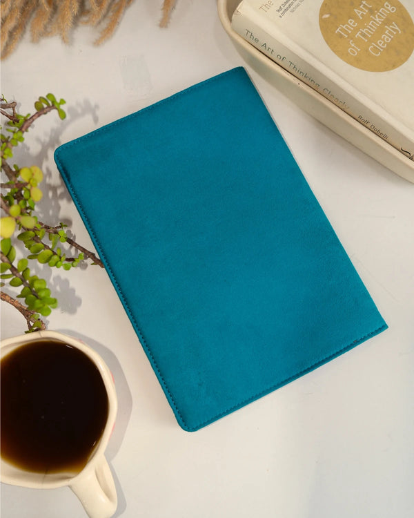 Blue notebook on a white surface with a cup of coffee and a plant