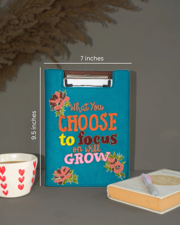 Blue clipboard with motivational quote and measurements on a dark surface