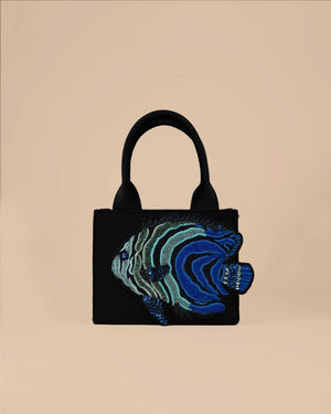 Black handbag with blue and green fish design on a beige background