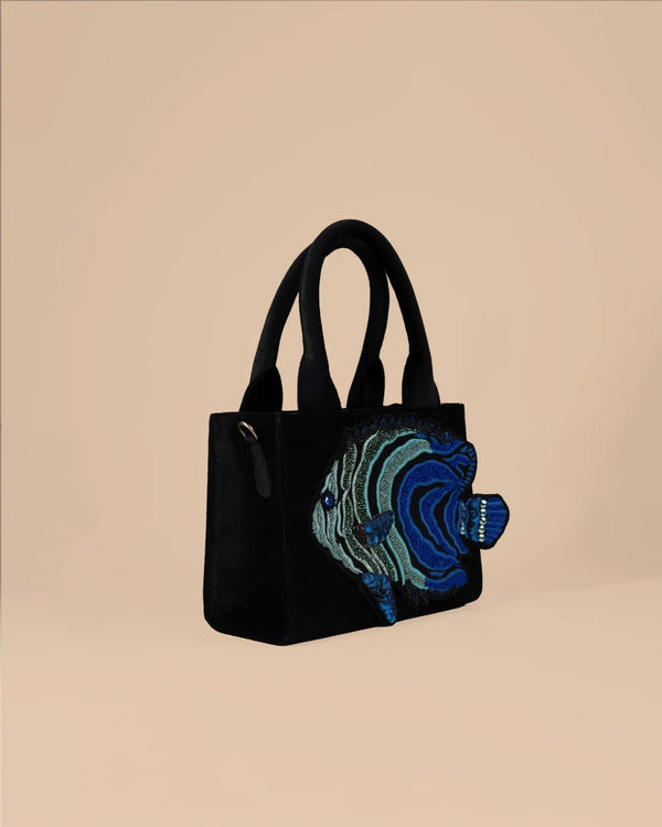 Black handbag with a blue and green fish design on a beige background