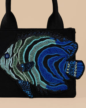Black handbag with blue and green fish design on a beige background