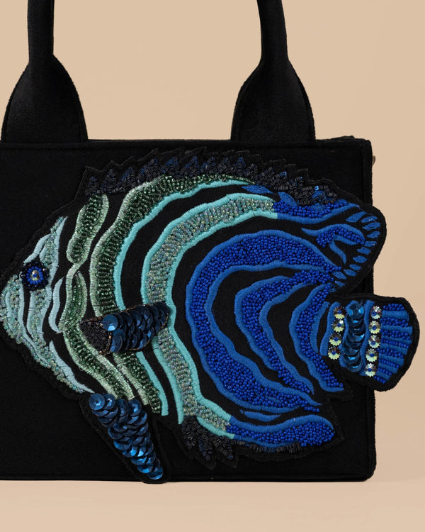 Black handbag with blue and green fish design on a beige background