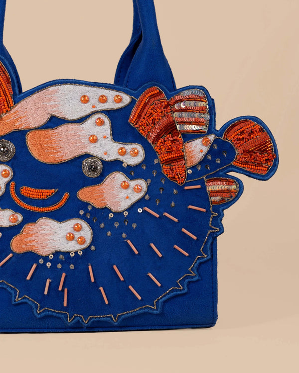 Blue handbag with colorful embroidered designs on a beige background